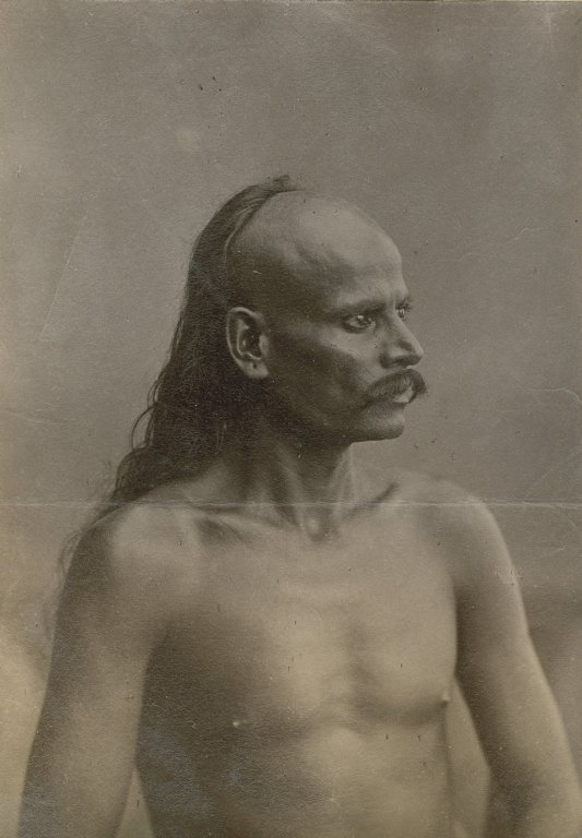 Indian man whose front scalp is shaved, with long hair in back.