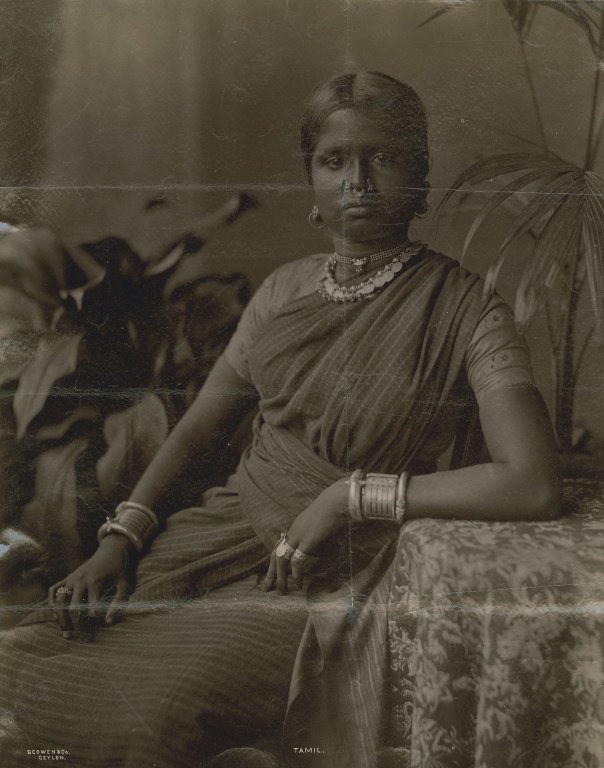 Portrait of seated woman, wearing abundant metal jewelry.