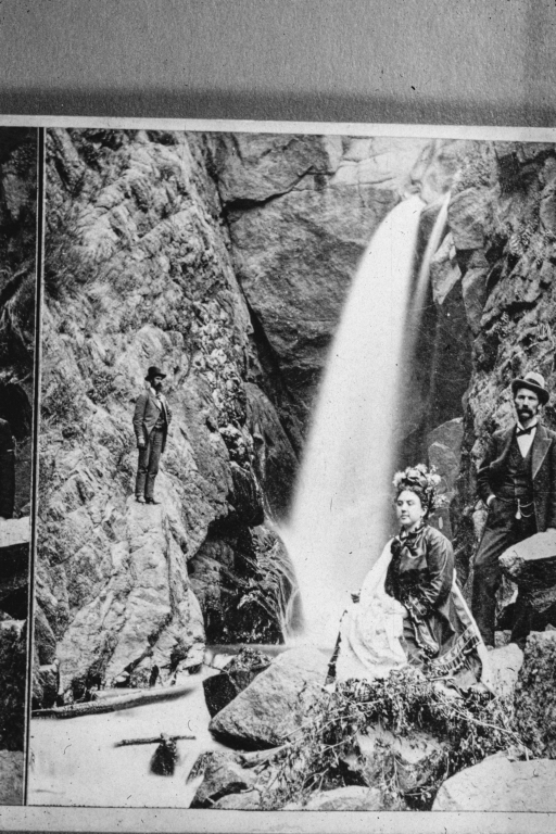 Two men and a woman with flowers in her hair next to a waterfall in Colorado